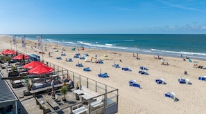 Una playa con sombrillas, sillas de playa y una terraza de madera con mesas y sillas.