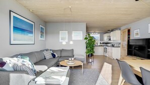 Uma sala de estar moderna com um sofá cinzento, uma mesa de centro e um espaço de refeições com uma mesa e cadeiras de madeira.