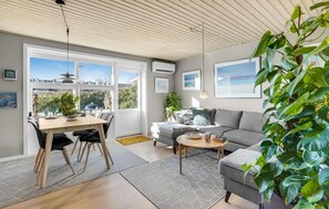 Un salon moderne avec un coin repas, de grandes fenêtres et une vue sur l’extérieur.