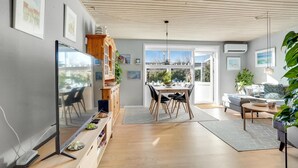 Uma sala de estar moderna com televisão, área de jantar e vista para o exterior.