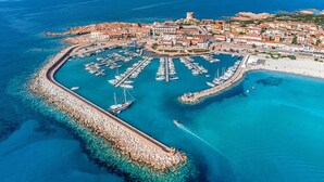 Luchtbeeld van een kustplaatsje met een jachthaven, een kasteelachtige constructie en een strand.