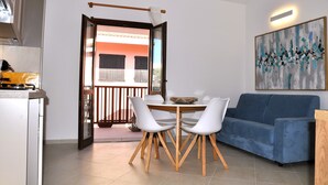 Een moderne woonkamer met een blauwe bank, witte stoelen, een eettafel en een balkon met een hekwerk.