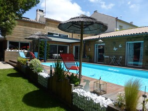 A backyard with a swimming pool, a wooden deck, and a covered patio area. - 130 m2 contemporary villa with swimming pool in enclosed wooded grounds (La Rochelle)