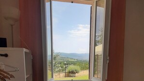 Una stanza con vista panoramica su un paesaggio, un termosifone, un tavolo con tovaglia fiorata e un armadietto bianco.