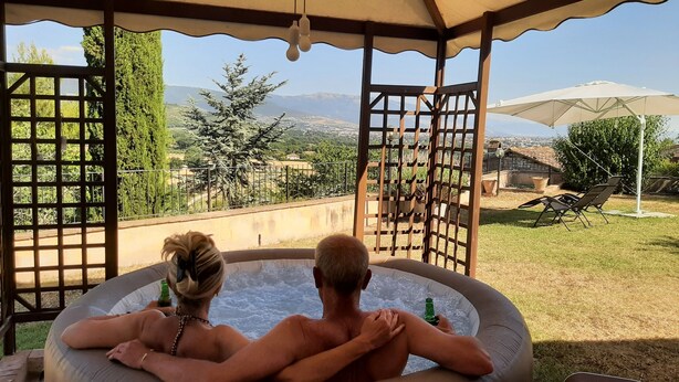 Una vasca idromassaggio con due persone sedute all'interno, affacciata su un giardino e una vista di montagne lontane.