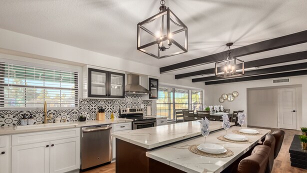 A modern kitchen with white cabinets, a stainless steel dishwasher, and a large island with a marble countertop. - 4BR w heated pool, basketball hoop, patio (Mesa)