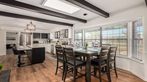 A modern kitchen with dark cabinetry, a central island, and a dining area with a large table and chairs. - 4BR w heated pool, basketball hoop, patio (Mesa)