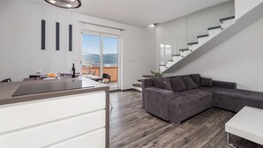 A modern kitchen with a built-in island, a grey sectional sofa, and a staircase with glass railings. - Awesome apartment in Kampor with WiFi (Kampor)