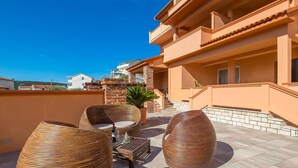 A rooftop terrace with wicker furniture, a potted plant, and a view of neighboring buildings. - Awesome apartment in Kampor with WiFi (Kampor)