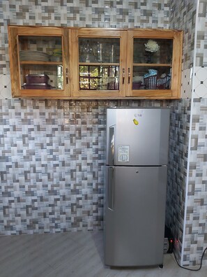Kitchen area with a refrigerator, cabinet, and tile-patterned walls.