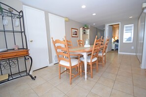 A dining area with a wooden table and chairs, a white door, and a kitchen visible in the background.
