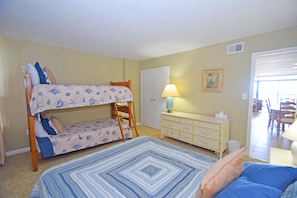 A room with bunk beds, a dresser, a lamp, and a door leading to another room.