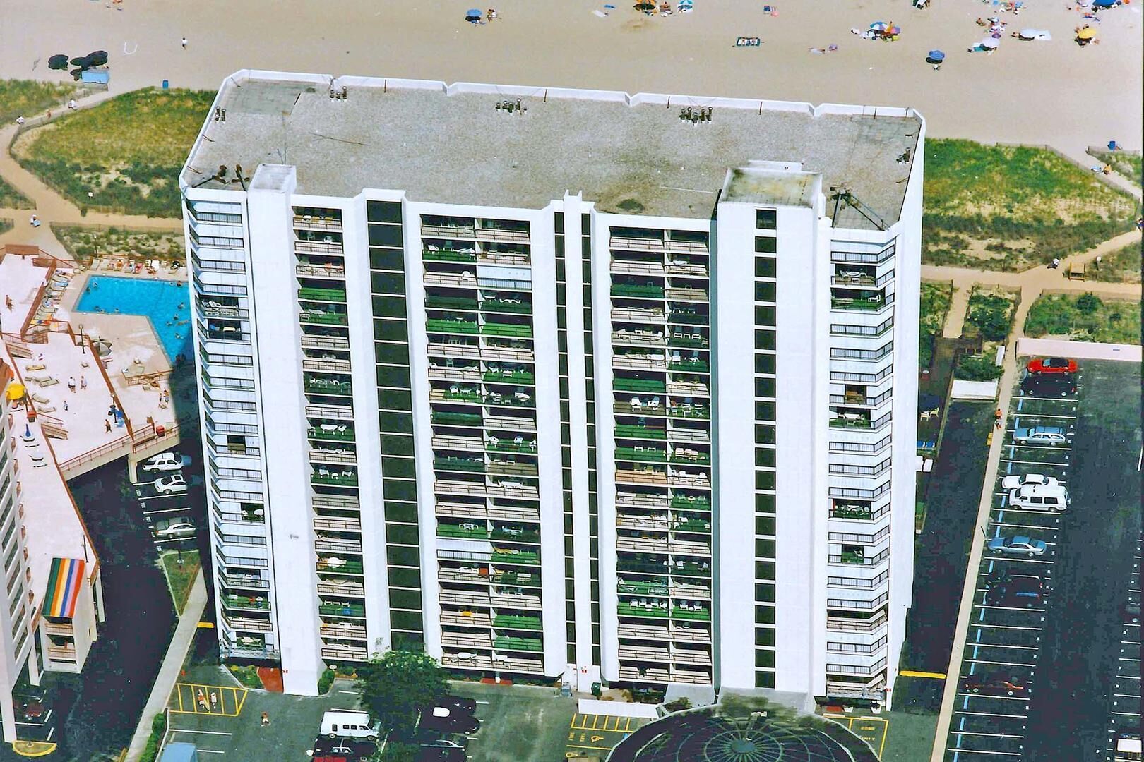 Ein Hochhaus mit mehreren Balkonen, einem Parkplatz und einem Strand im Hintergrund.