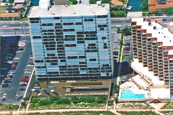 A high-rise building with a modern glass facade, a parking lot, and a swimming pool area.