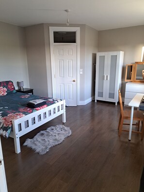 A bedroom with a bed, a desk, a wardrobe, and a fluffy rug.