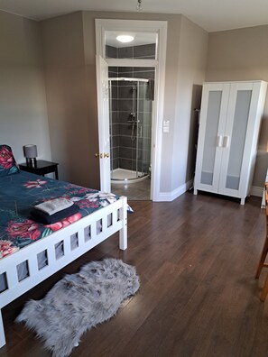 A bedroom with a bed, a fluffy rug, a nightstand, a lamp, a wardrobe, and a shower area.