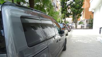 A grey van parked on a paved sidewalk next to a building with a white exterior.