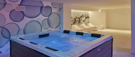 Een moderne spa met een bubbelbad, een muur met ronde patronen en een ontspanningsruimte met stoelen.