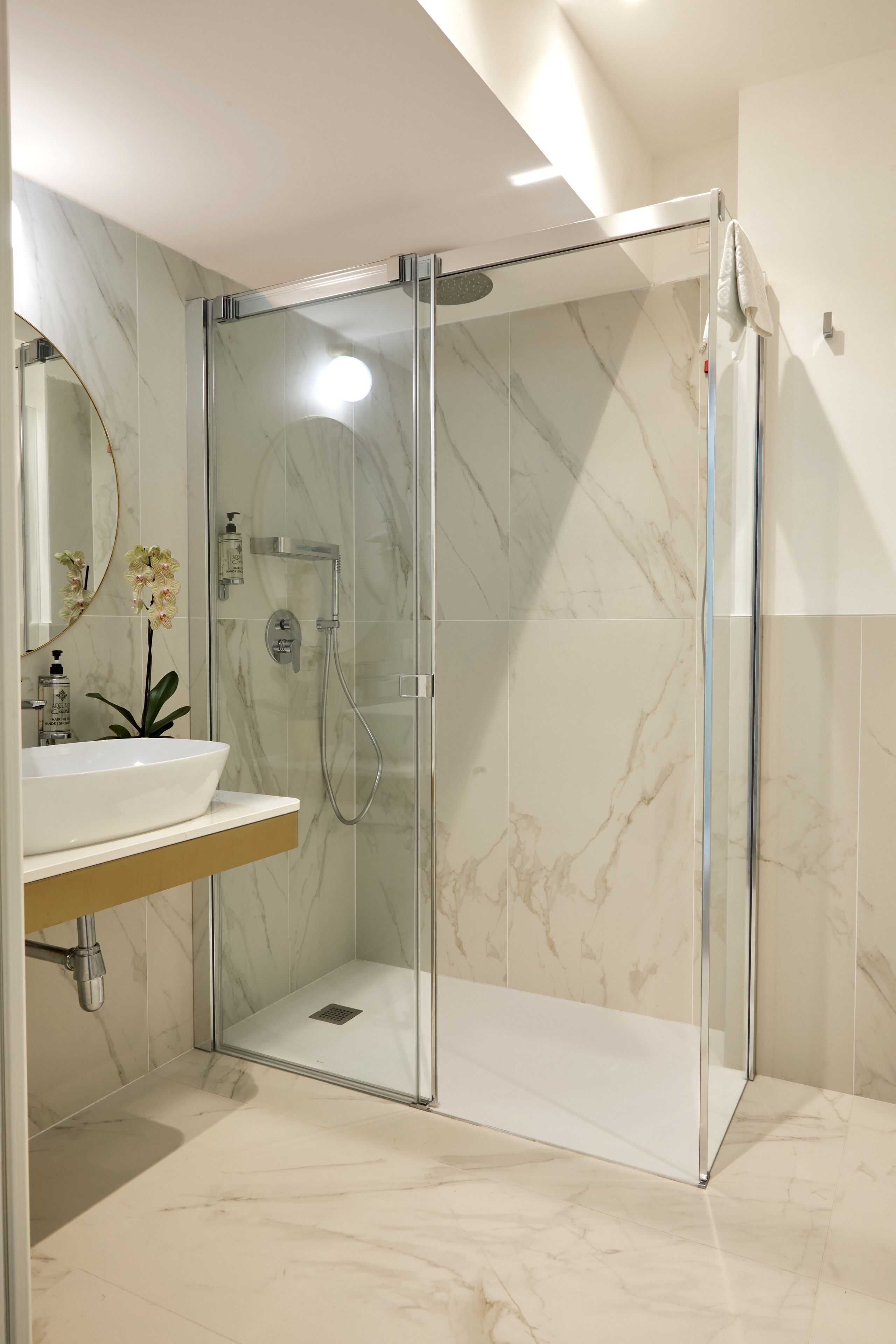 A modern bathroom with a glass-enclosed shower, a marble-tiled floor, and a sink with a mirror above it.