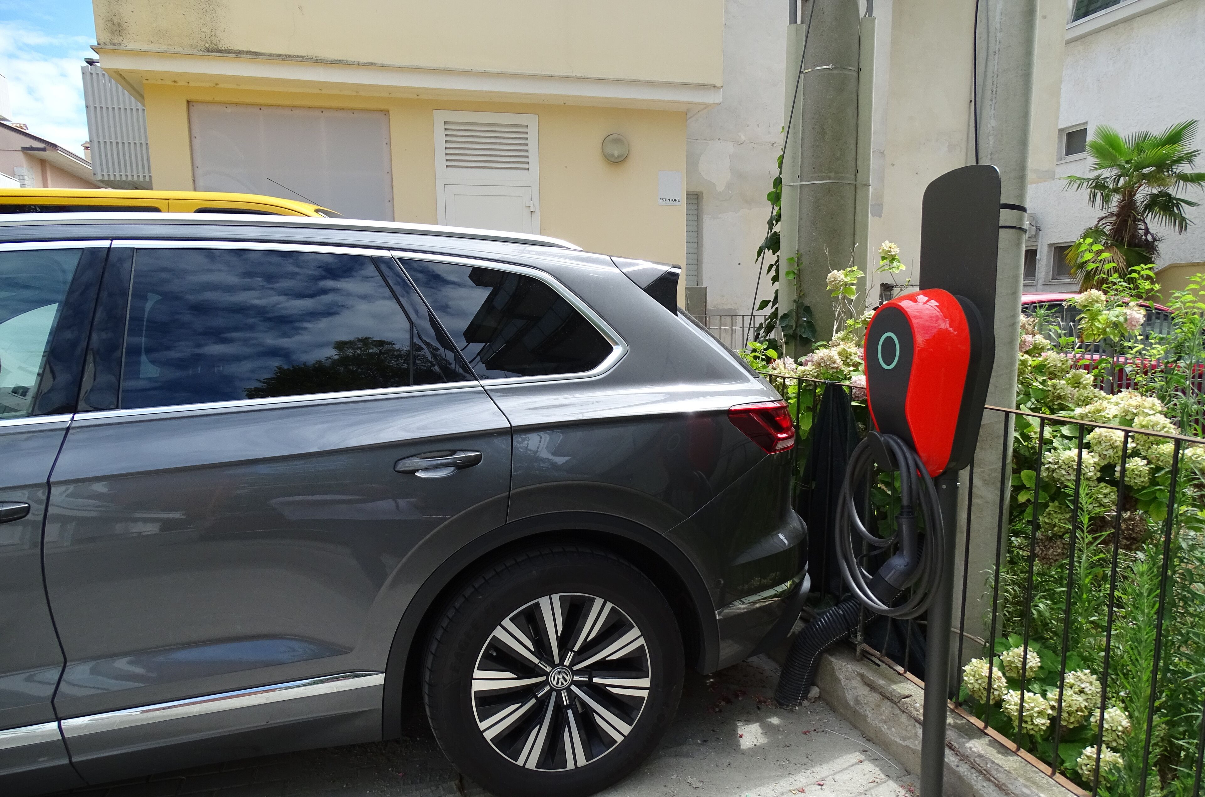 Un SUV grigio parcheggiato accanto a un edificio con un idrante rosso e un giardino con fiori bianchi.