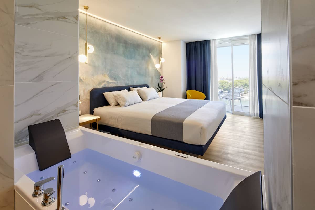 A modern hotel room with a large bed, a bathtub, and a view of the city.