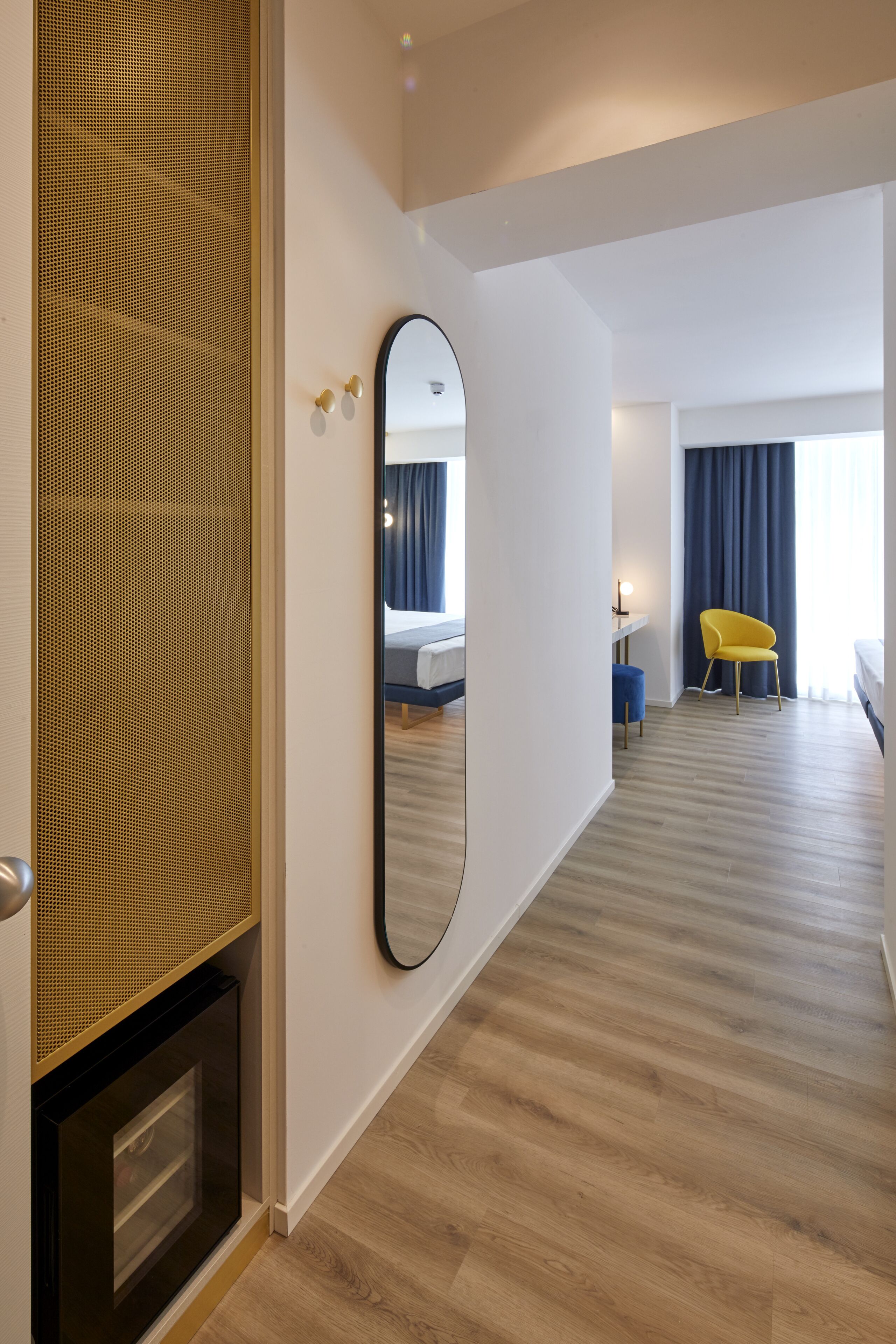 Une chambre d’hôtel avec un grand miroir, un lit, un bureau, une chaise et une petite table avec une lampe.