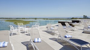 Zona de piscina en la azotea con sillones de descanso y una barandilla de cristal con vista a un cuerpo de agua.