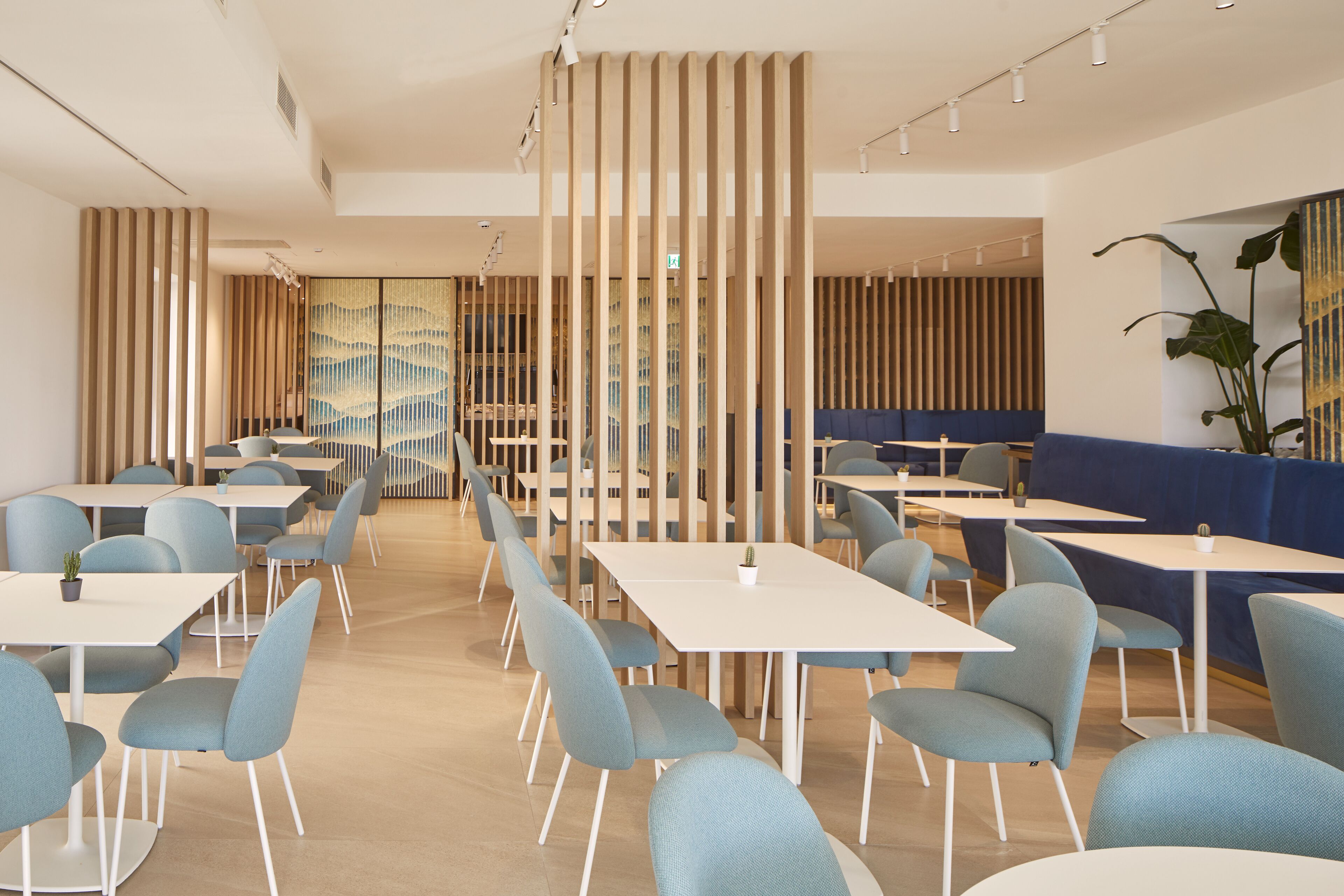 Un comedor moderno con mesas y sillas, un área de asientos con cojines azules, y listones verticales de madera.