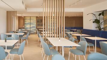 Un comedor moderno con mesas y sillas, un área de asientos con cojines azules, y listones verticales de madera.