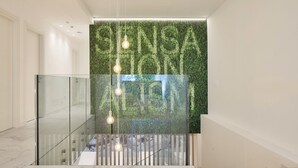 Un interior moderno con barandilla de vidrio, pared verde con líneas verticales y lámparas colgantes.