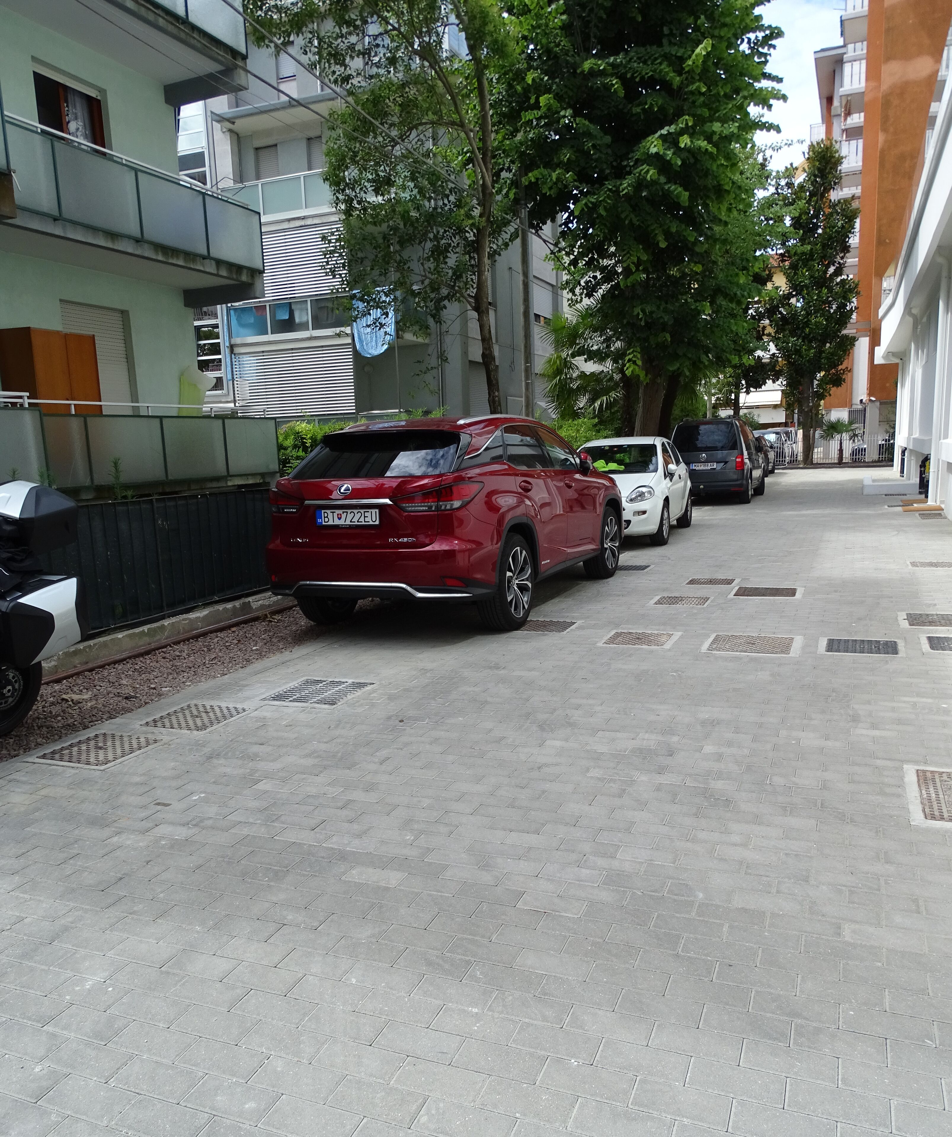 Un SUV rosso parcheggiato su strada asfaltata, con un edificio a sinistra e alberi a destra.