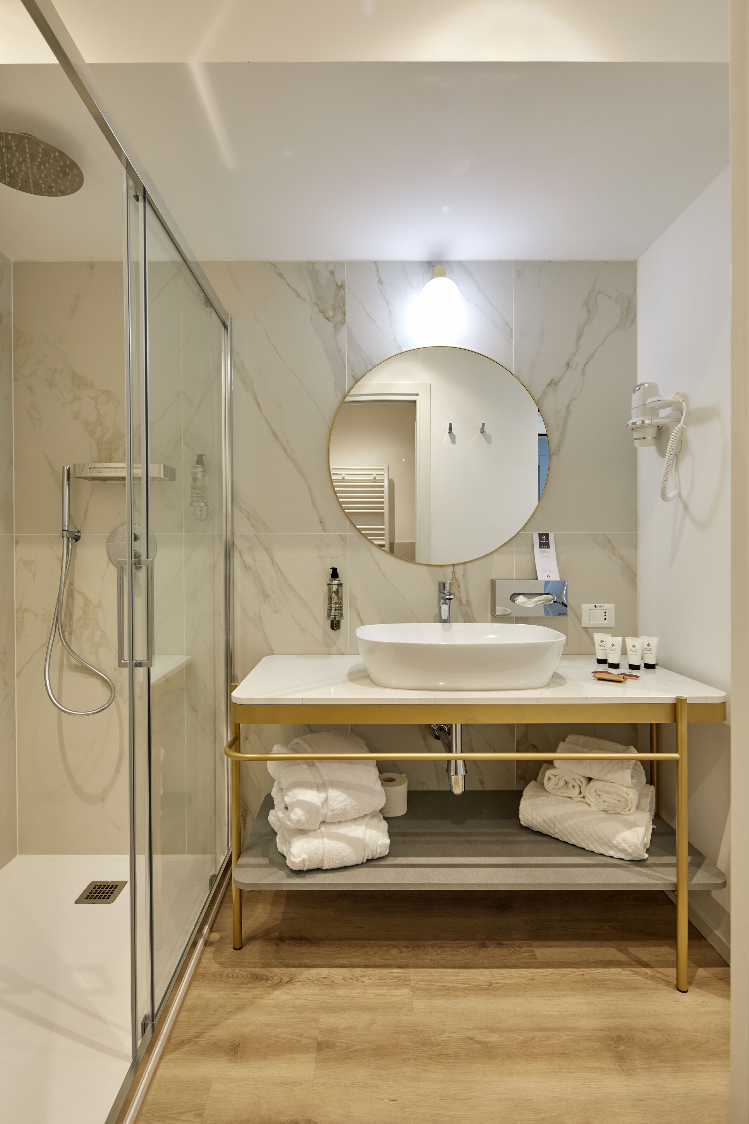 A modern bathroom with a glass-enclosed shower, a white sink, and a gold-framed vanity.
