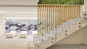 A modern interior with a marble staircase, a seating area with white sofas, and a wall with a naturalistic mural.