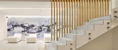 Un interior moderno con una escalera de mármol, una zona de estar con sofás blancos y una pared con un mural naturalista.