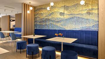 A modern restaurant with blue upholstered booths, round tables, and a decorative wall with a wave pattern.