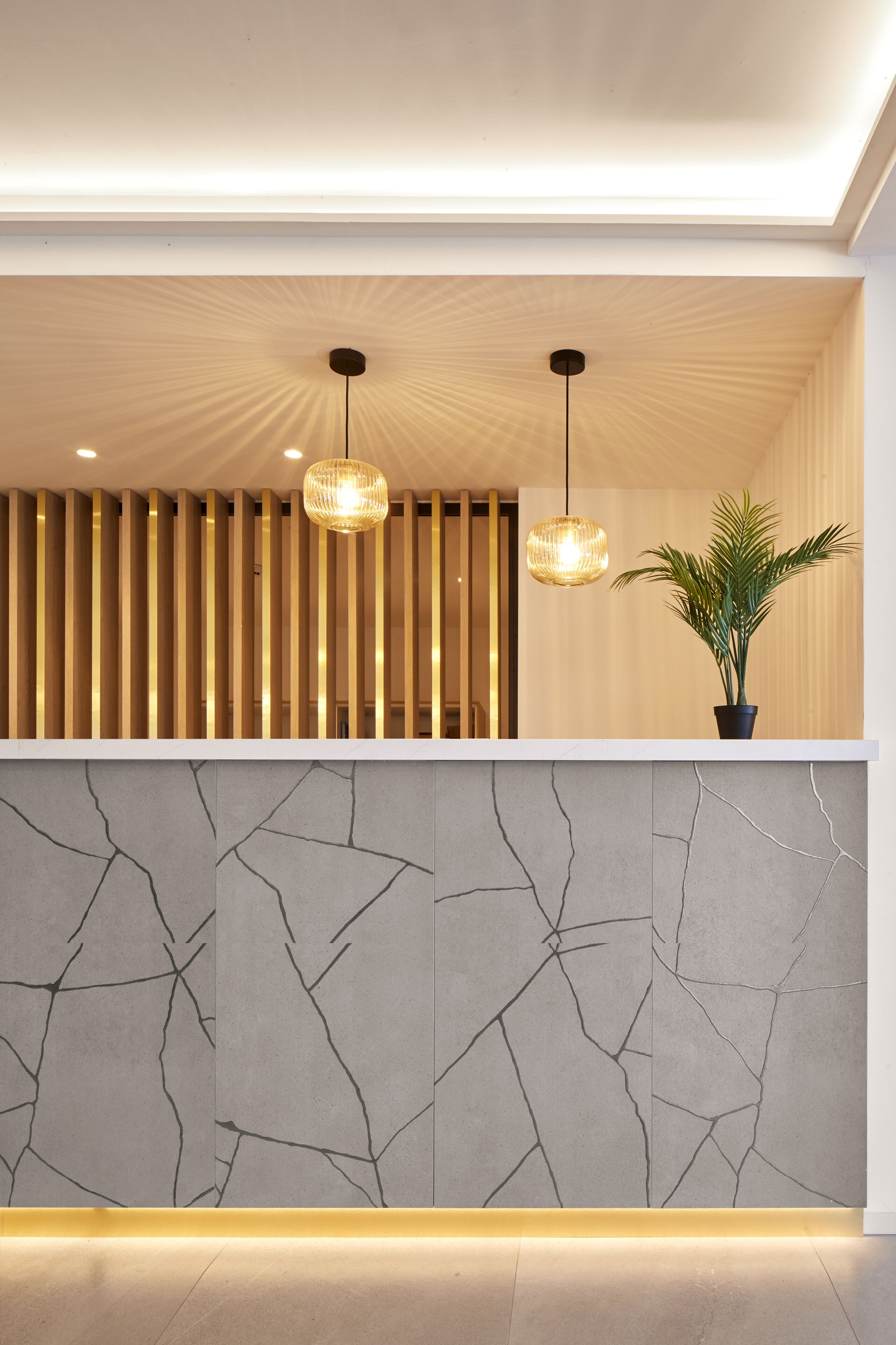 Ein Empfangsbereich mit modernem Design, der eine Wand aus Holzleisten, eine Marmorwand mit Rissen und zwei Pendelleuchten zeigt.