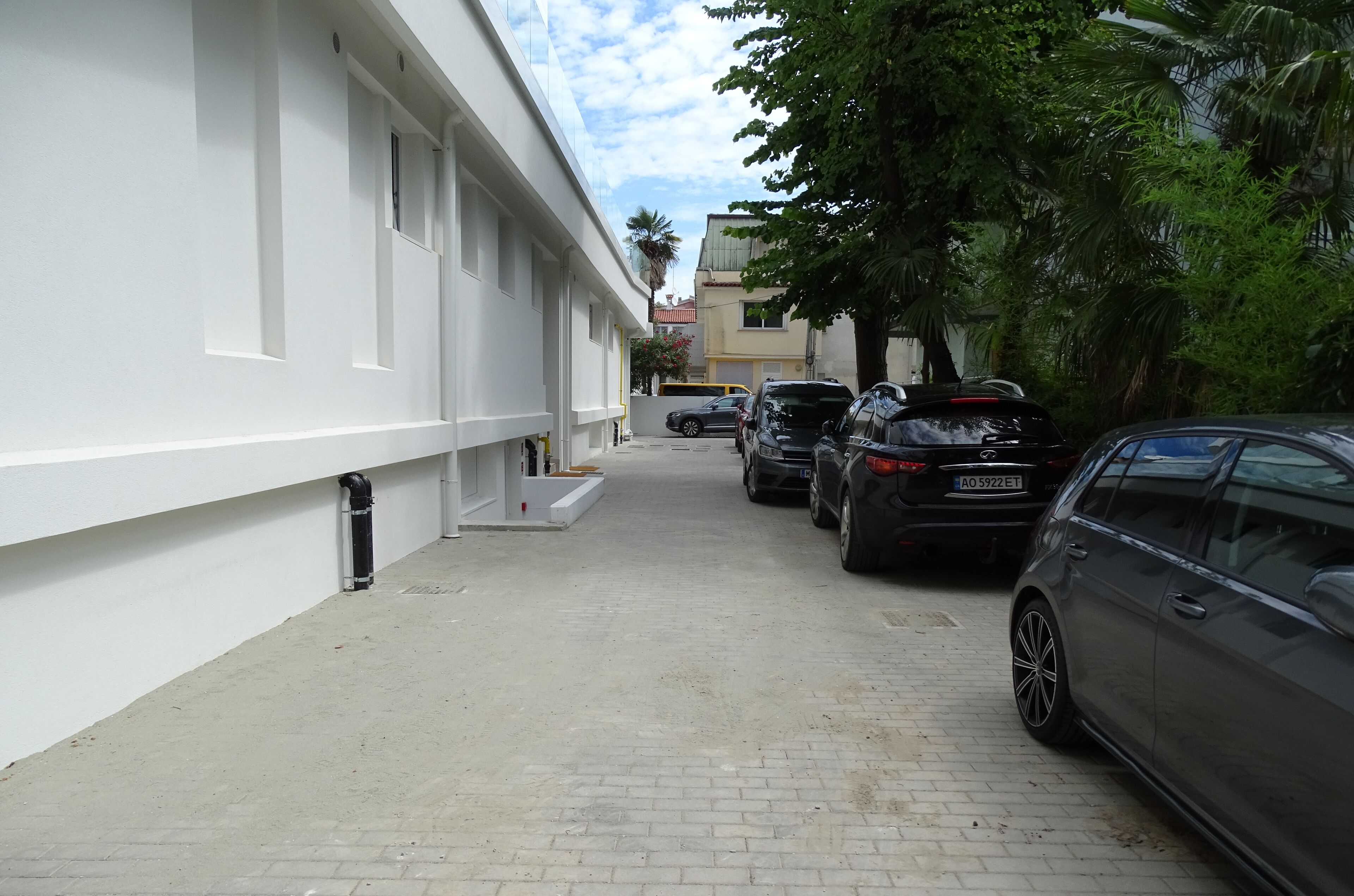 A narrow street with parked cars and a white building with multiple windows.