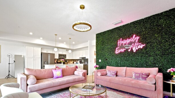Una sala moderna con dos sofás rosados, una mesa de centro de cristal y una pared verde con un letrero de neón.