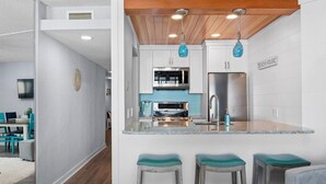 Una cucina moderna con mobili bianchi, un'isola centrale con sgabelli e un cartello con scritto "BEACH HOUSE".