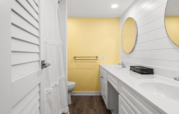 Un baño con pared de acento amarilla, un lavamanos blanco y un espejo redondo.