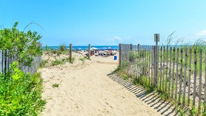 Un sentiero sabbioso che conduce a una spiaggia con ombrelloni e persone.