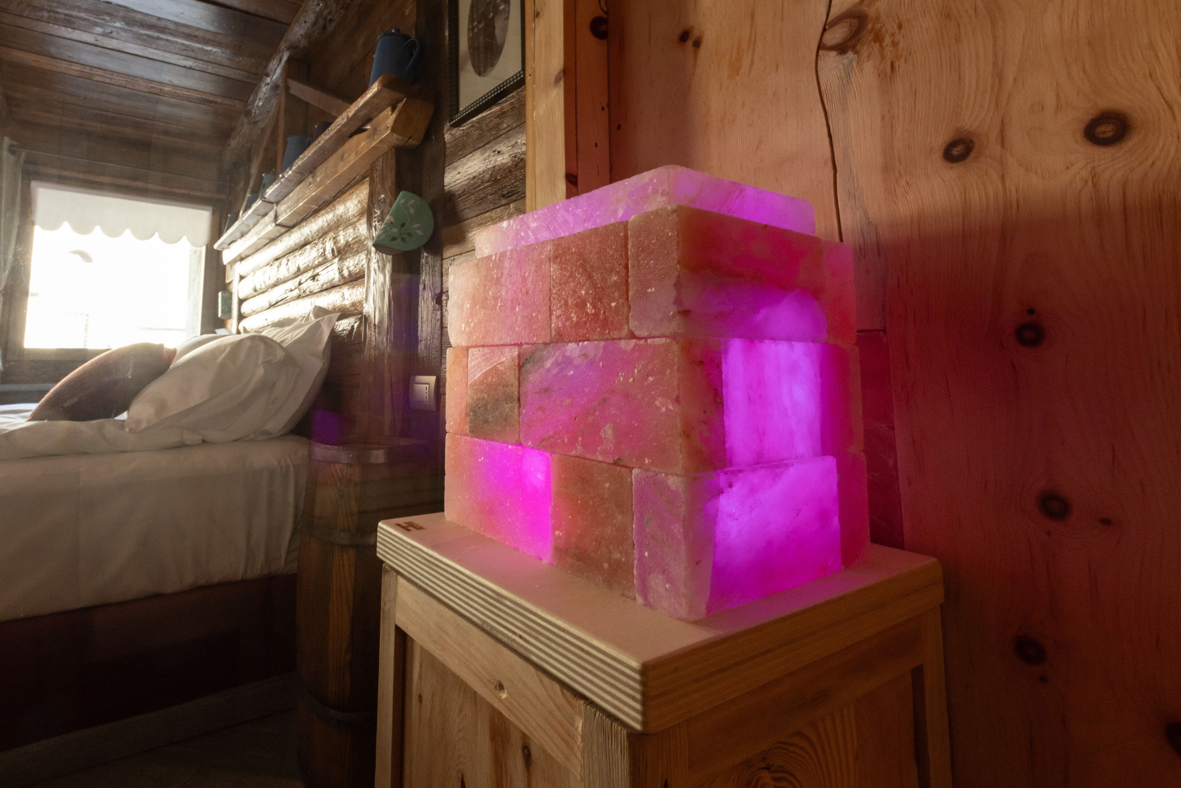 A wooden cabin interior with a bed, a wooden cabinet, and a glowing pink object on a table.