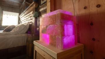 A wooden cabin interior with a bed, a wooden cabinet, and a glowing pink object on a table.
