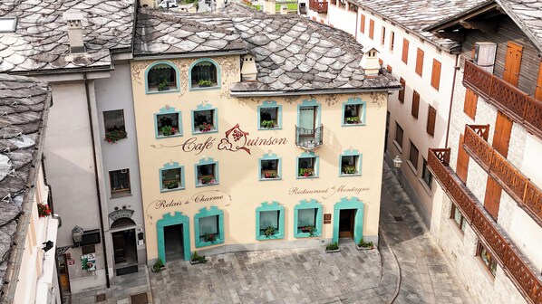 Um edifício com várias janelas, algumas com plantas, e uma placa que diz 'Café Quinson'.
