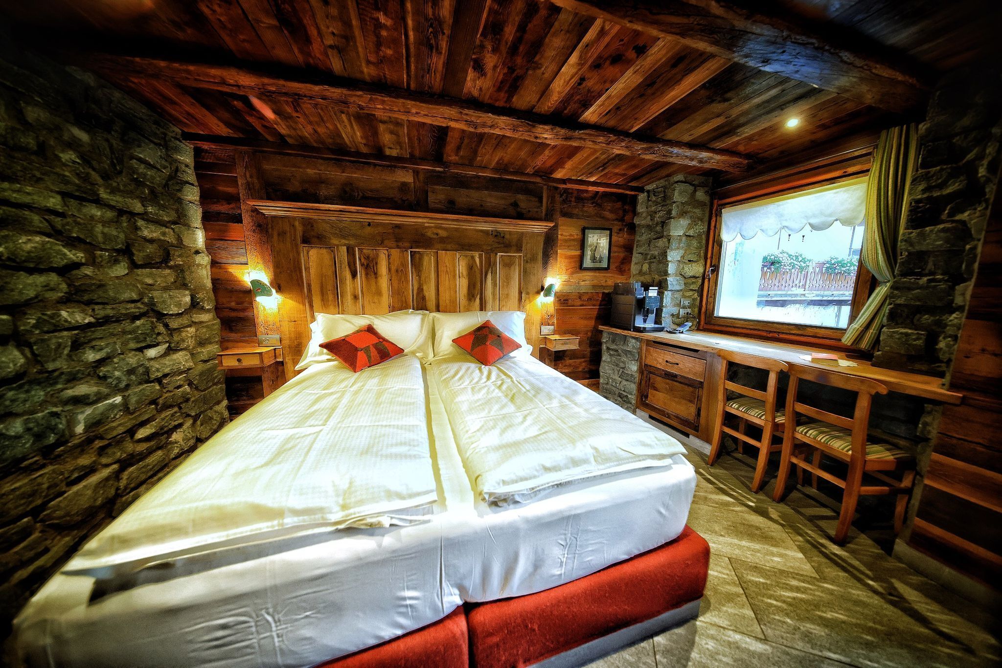 Een houten slaapkamer met een bed, een bureau en een stenen muur.