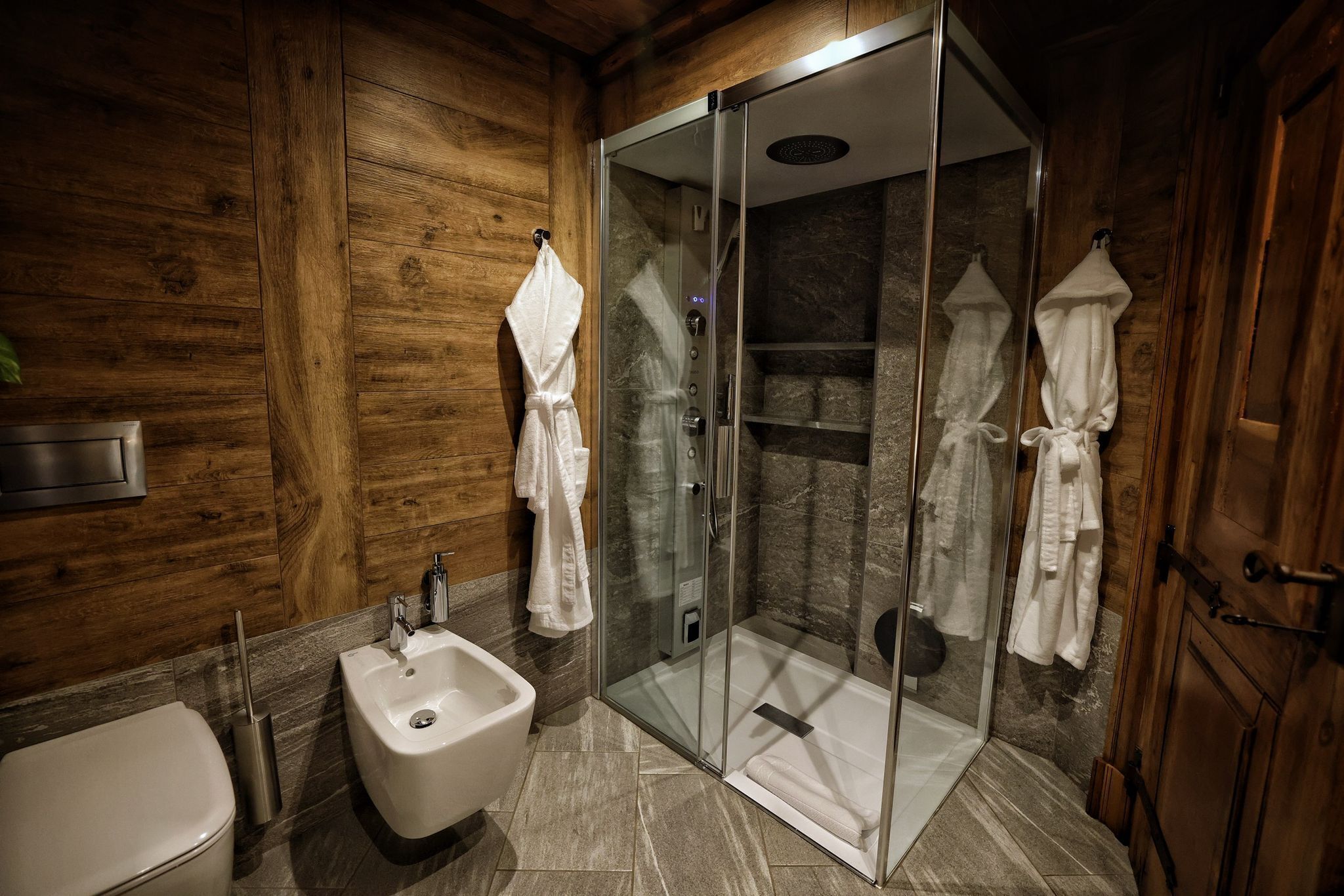Une salle de bain moderne dotée d’une douche à parois de verre, d’un bidet et de lambris en bois.