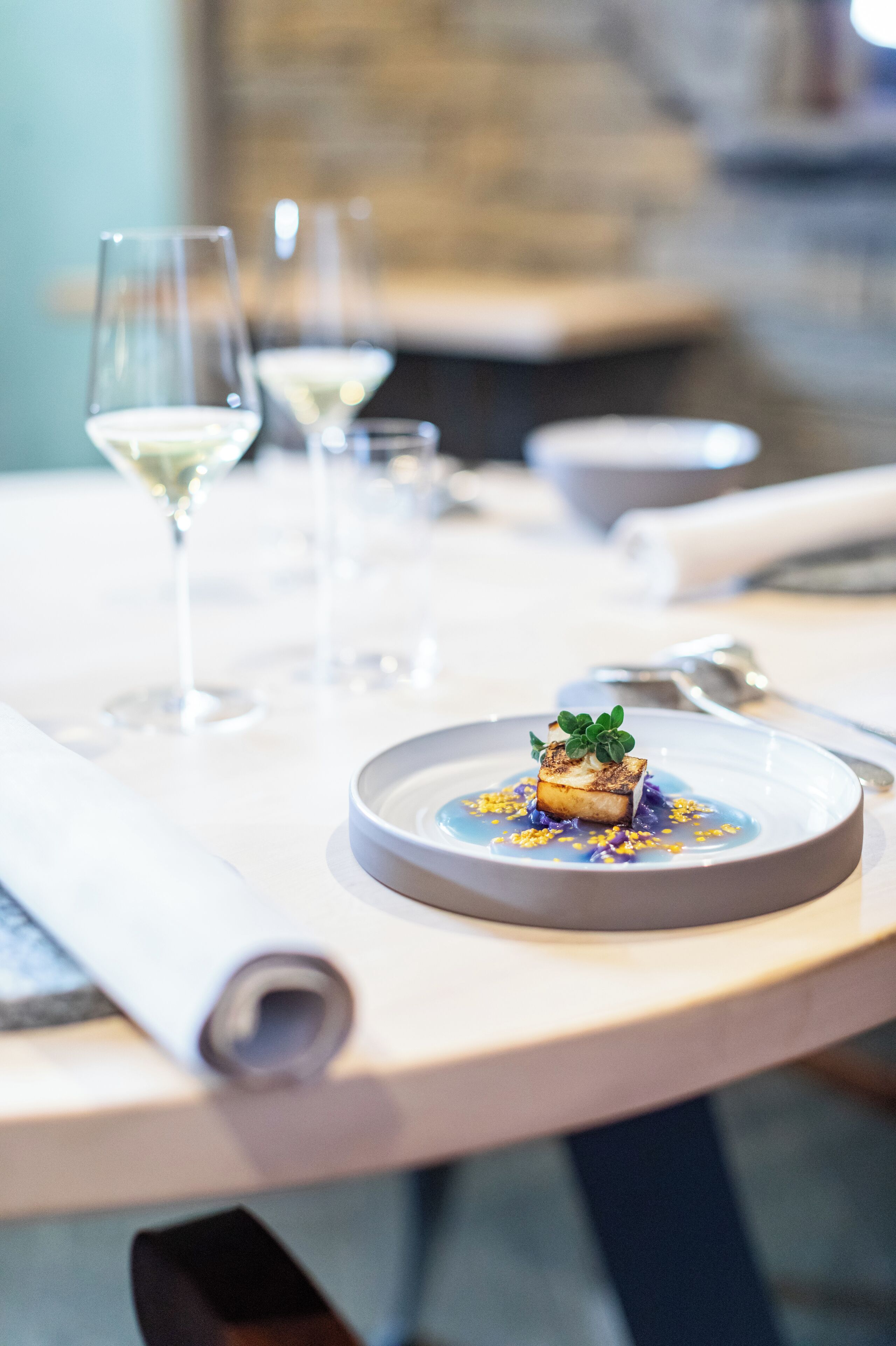A dining table with a plate of food, a glass of white wine, and a napkin.