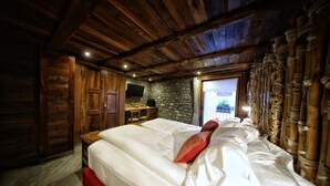 Ein Schlafzimmer in einer Holzhütte mit einer Steinsäule, einem Bett mit weißer Bettwäsche und einer kleinen Schreibtischzeile.