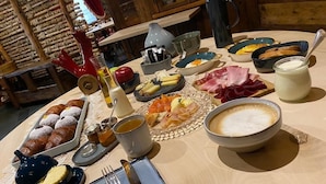Ein reichhaltiges Frühstücksbuffet mit verschiedenen Backwaren, Fleisch, Käse und Getränken auf einem Holztisch.