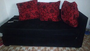 A black sofa with red floral cushions against a plain wall and patterned floor tiles. - VIV HAVEN (Nairobi)